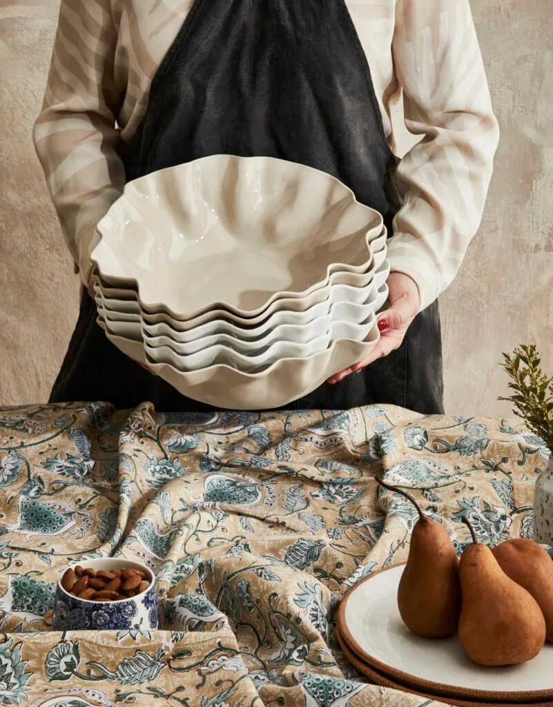 A person holding a collection of wavy ceramic bowls.