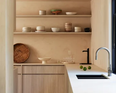 A kitchen, which leads into a butler's pantry, with a curved kitchen mixer tap positioned next to a sink and open shelves on the walls, where pottery is displayed.
