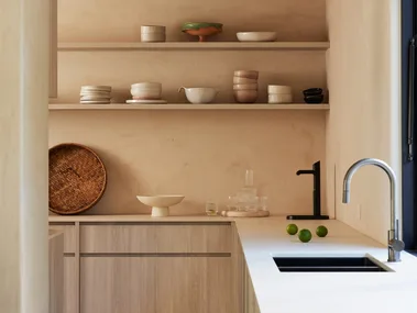 A kitchen, which leads into a butler's pantry, with a curved kitchen mixer tap positioned next to a sink and open shelves on the walls, where pottery is displayed.