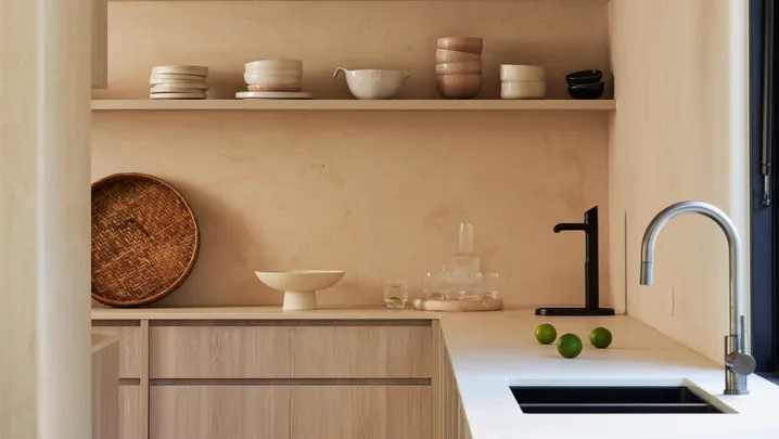 A kitchen, which leads into a butler's pantry, with a curved kitchen mixer tap positioned next to a sink and open shelves on the walls, where pottery is displayed.