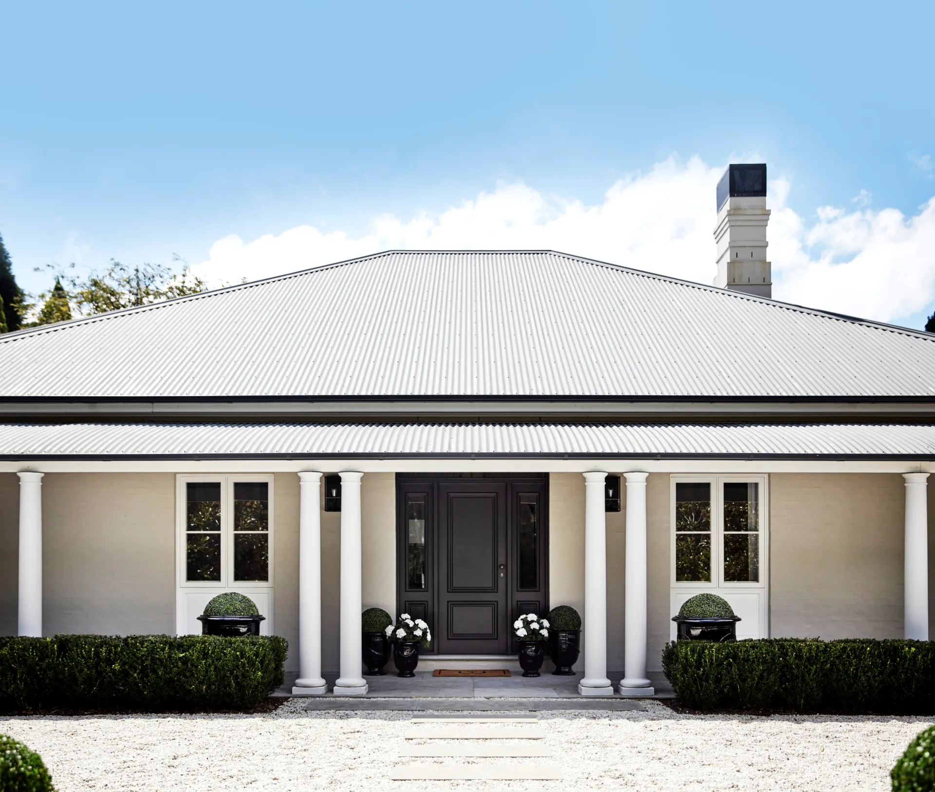 The exterior of a country house with white pillars and garden hedges.