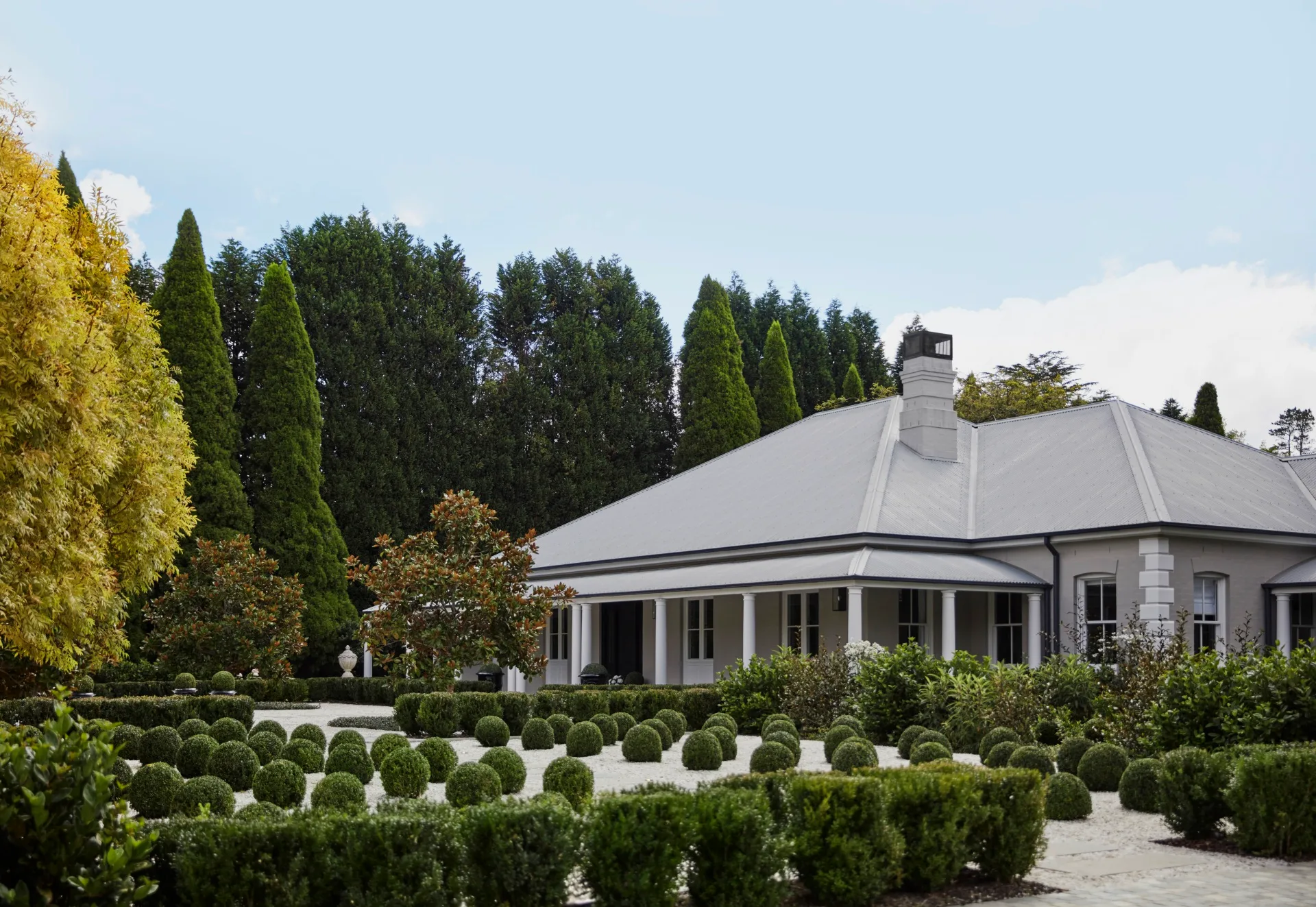 A country house surrounded by rounded topiary plants.