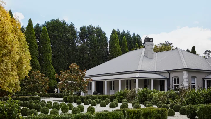 A country house surrounded by rounded topiary plants.