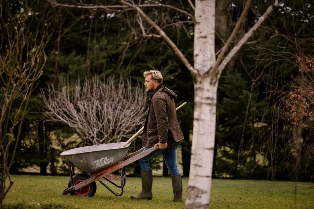 Gardener Ashley James pushing a wheelbarrow through a garden.