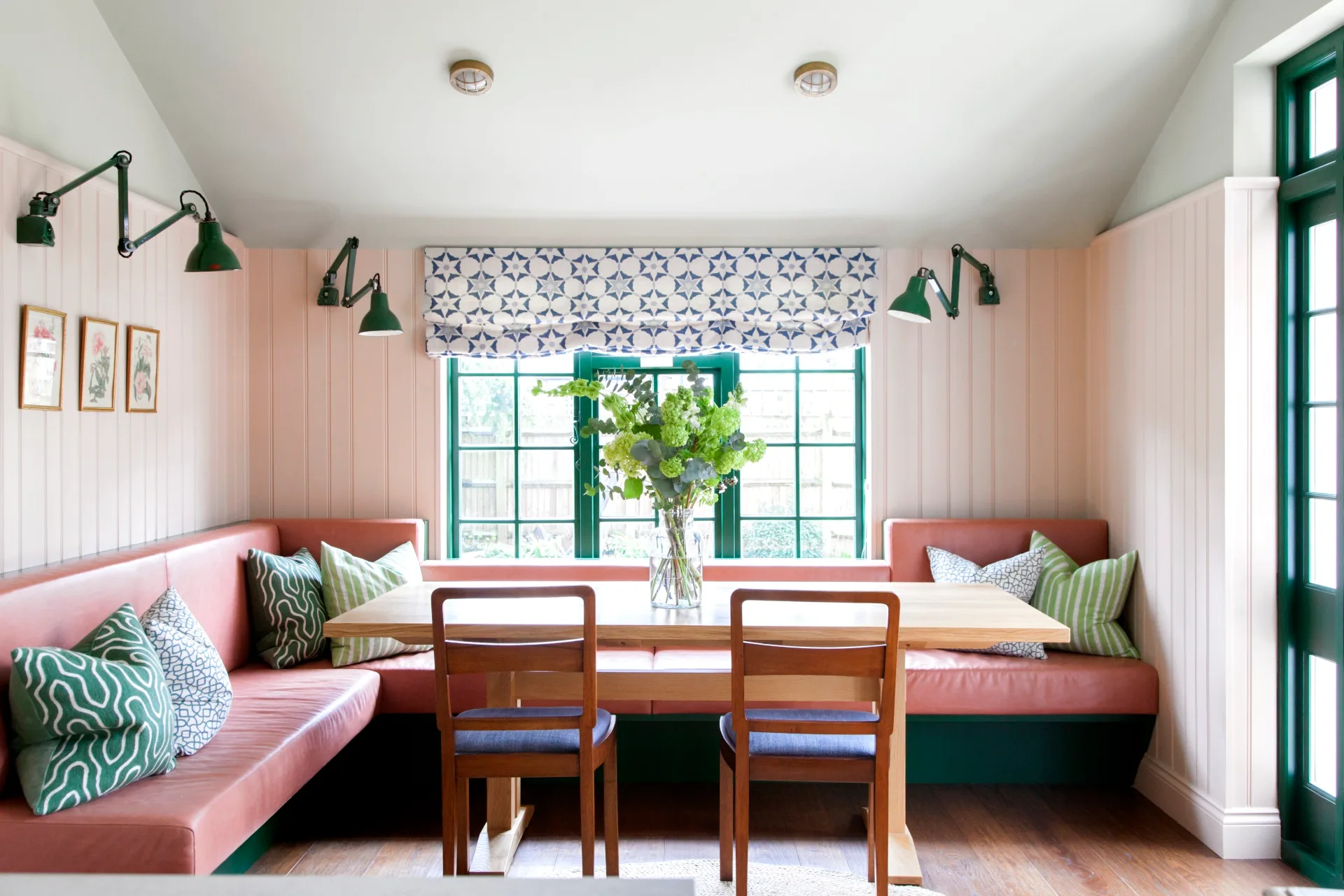 Pink banquette seating around a dining table with green wall lamps.