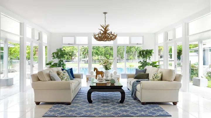 A modern country living room with white and blue furnishings overlooking the pool.