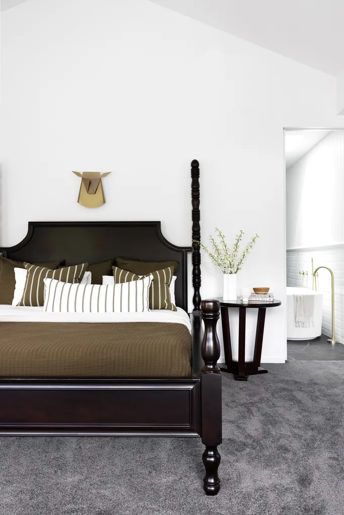 A main bedroom with a timber bed and grey carpets.