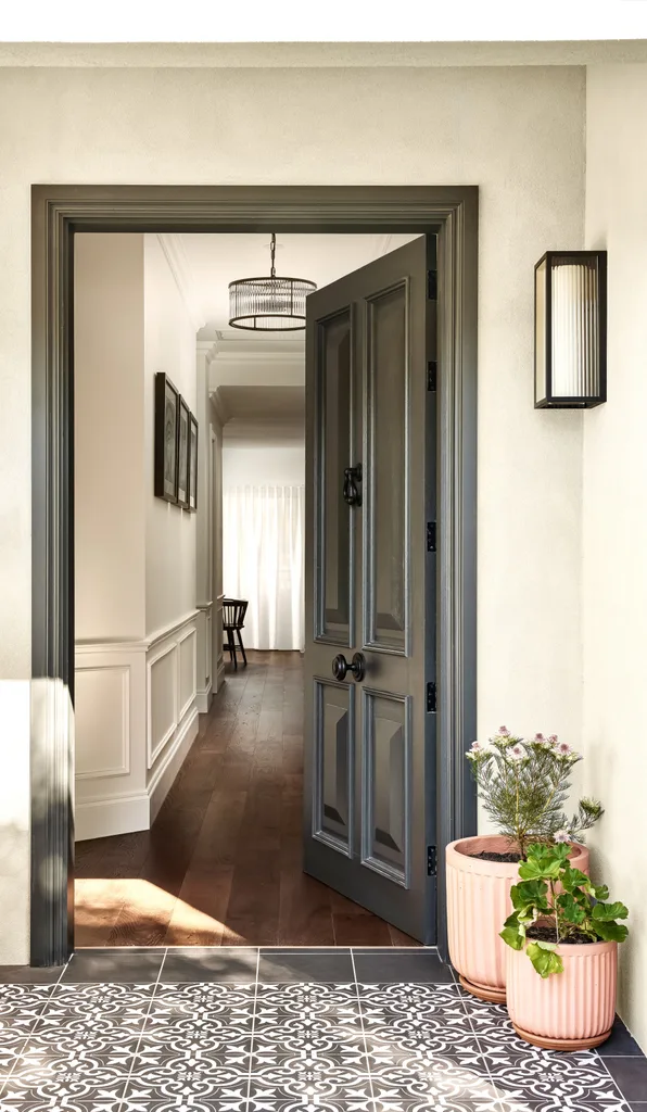 An entryway with mosaic black and white tiles and a door with wainscoting style panels.