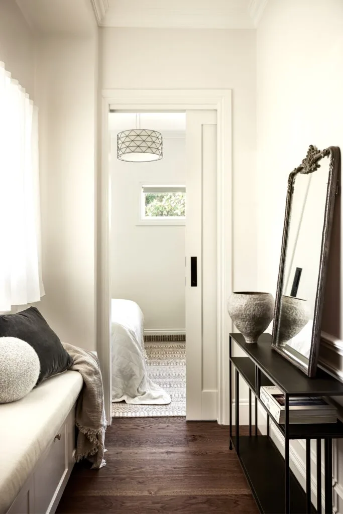 A hallway with a vintage-style mirror and window bench.