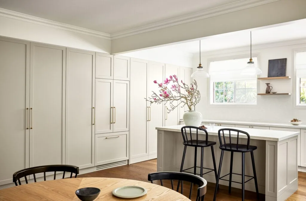 A modern neutral kitchen with shaker style cabinets, an island and timber table.