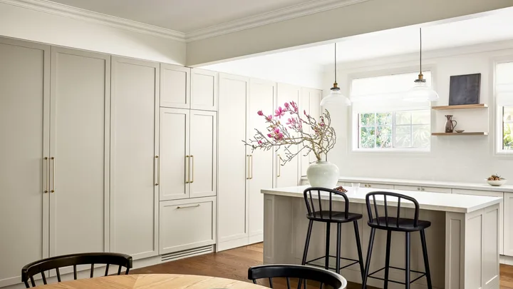 A modern neutral kitchen with shaker style cabinets, an island and timber table.