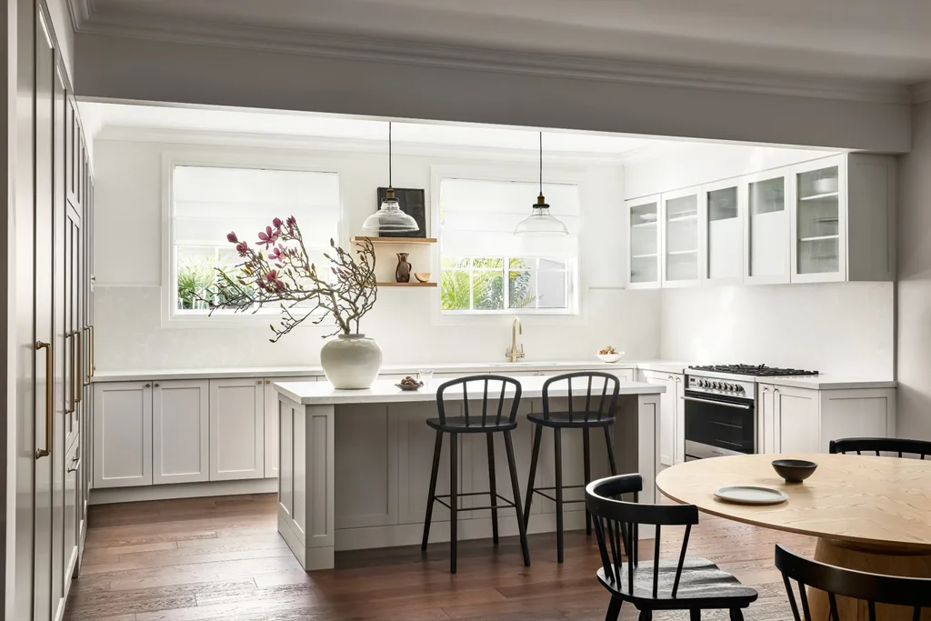 A spacious neutral kitchen with an island bench, black stools and shaker cabinets.