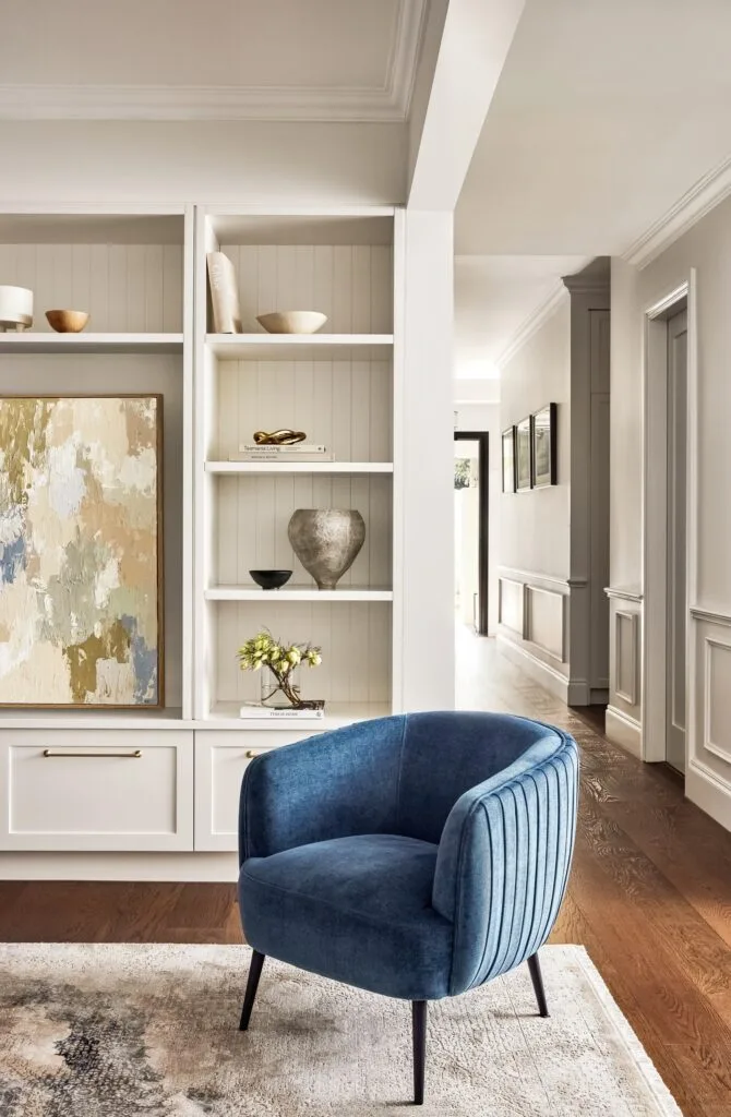 A living room area with VJ panel walls, a round blue armchair and open shelves.