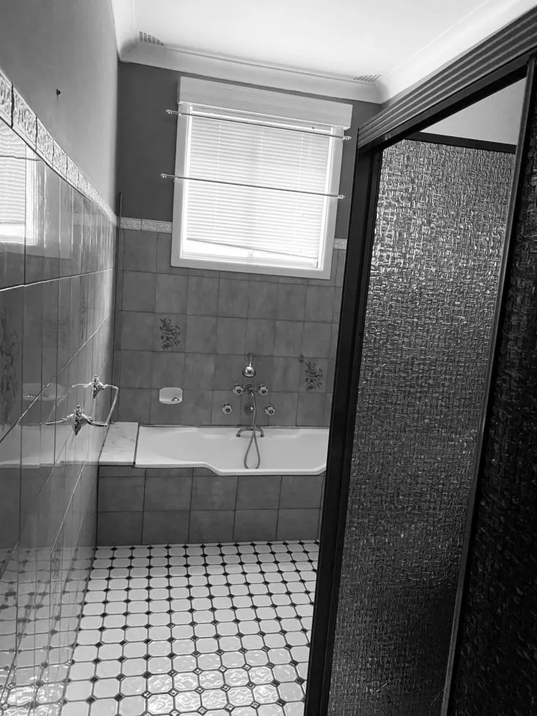 A dated bathroom with a frosted shower screen and black and white tiles.