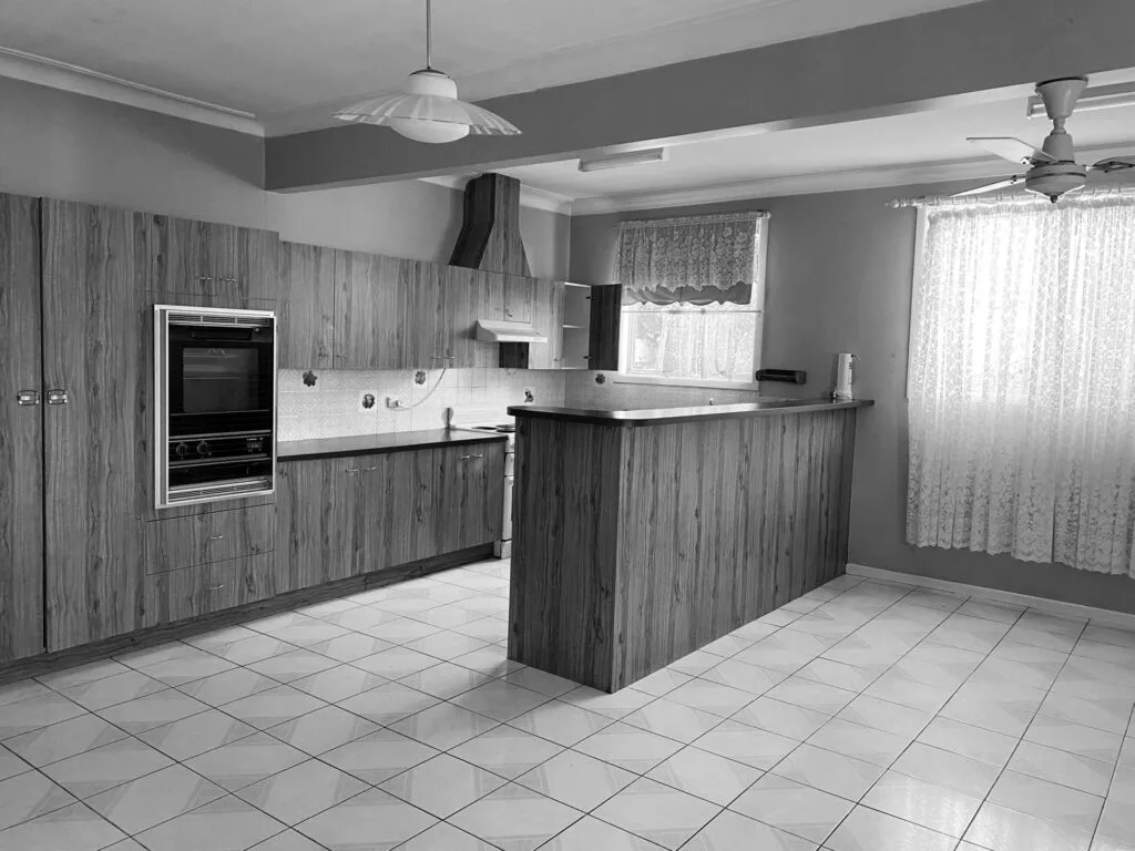 A dated kitchen with wood-style panelling and lace curtains.