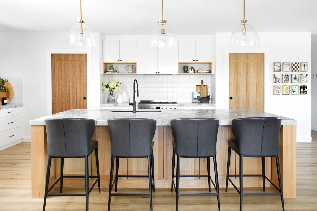 A modern white and timber kitchen with a marble island with black stools.