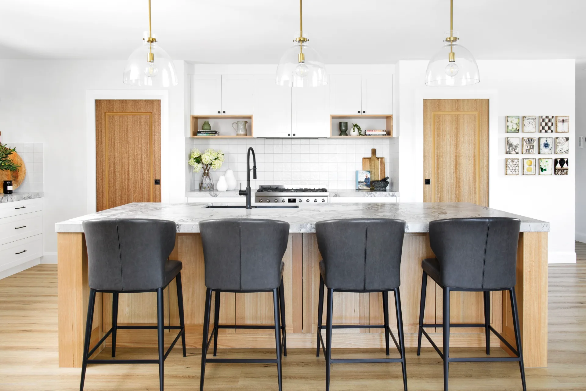 A modern white and timber kitchen with a marble island with black stools.