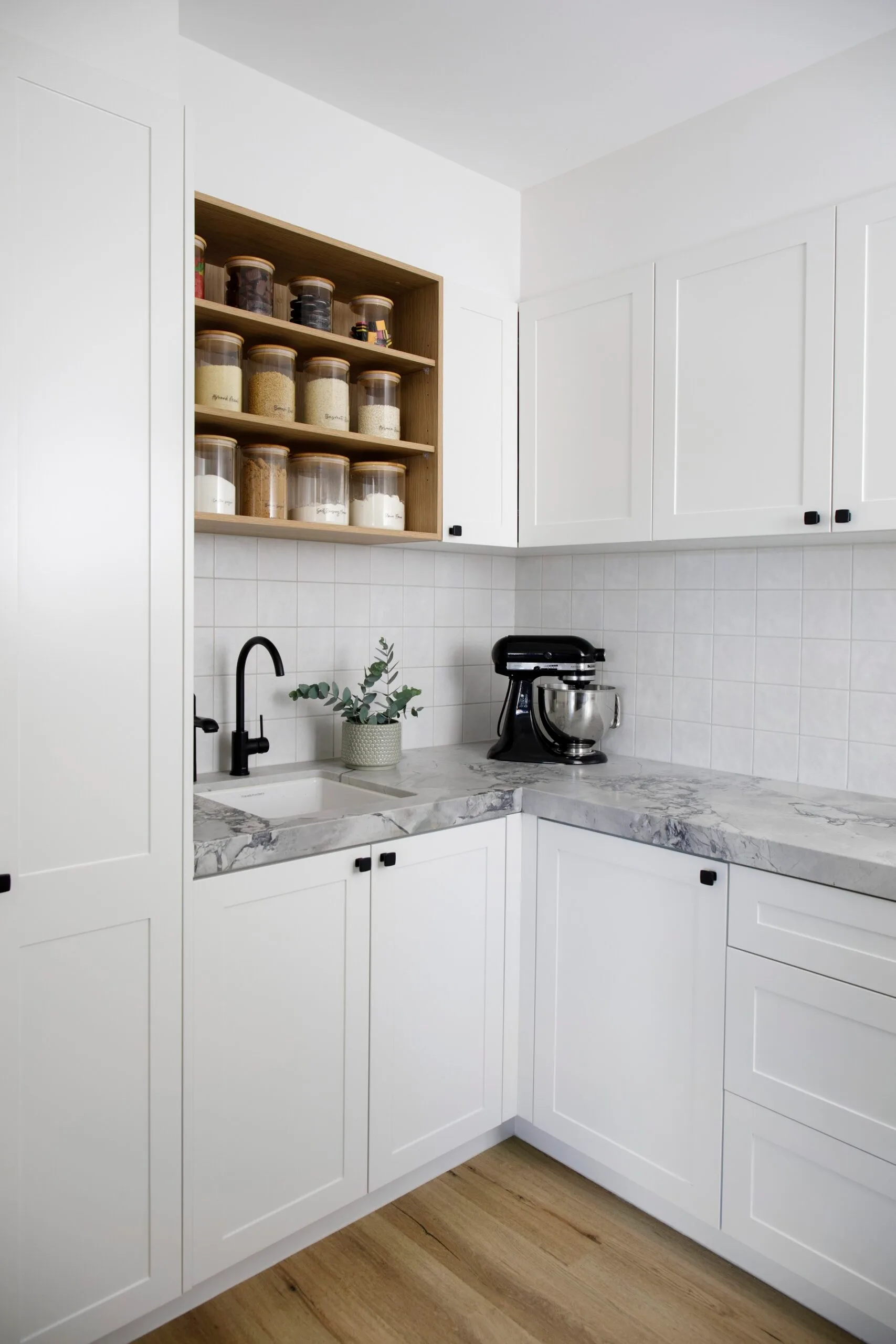 A white butler's pantry with marble-style benchtops and open spice shelves.