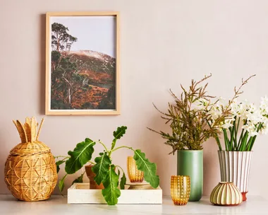 A console with a tray, wicker pineapple and vases of flowers.