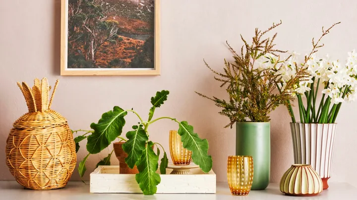 A console with a tray, wicker pineapple and vases of flowers.
