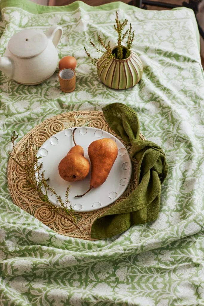 A tablescape with a patterned green tablecloth, rattan placemat and ceramics.