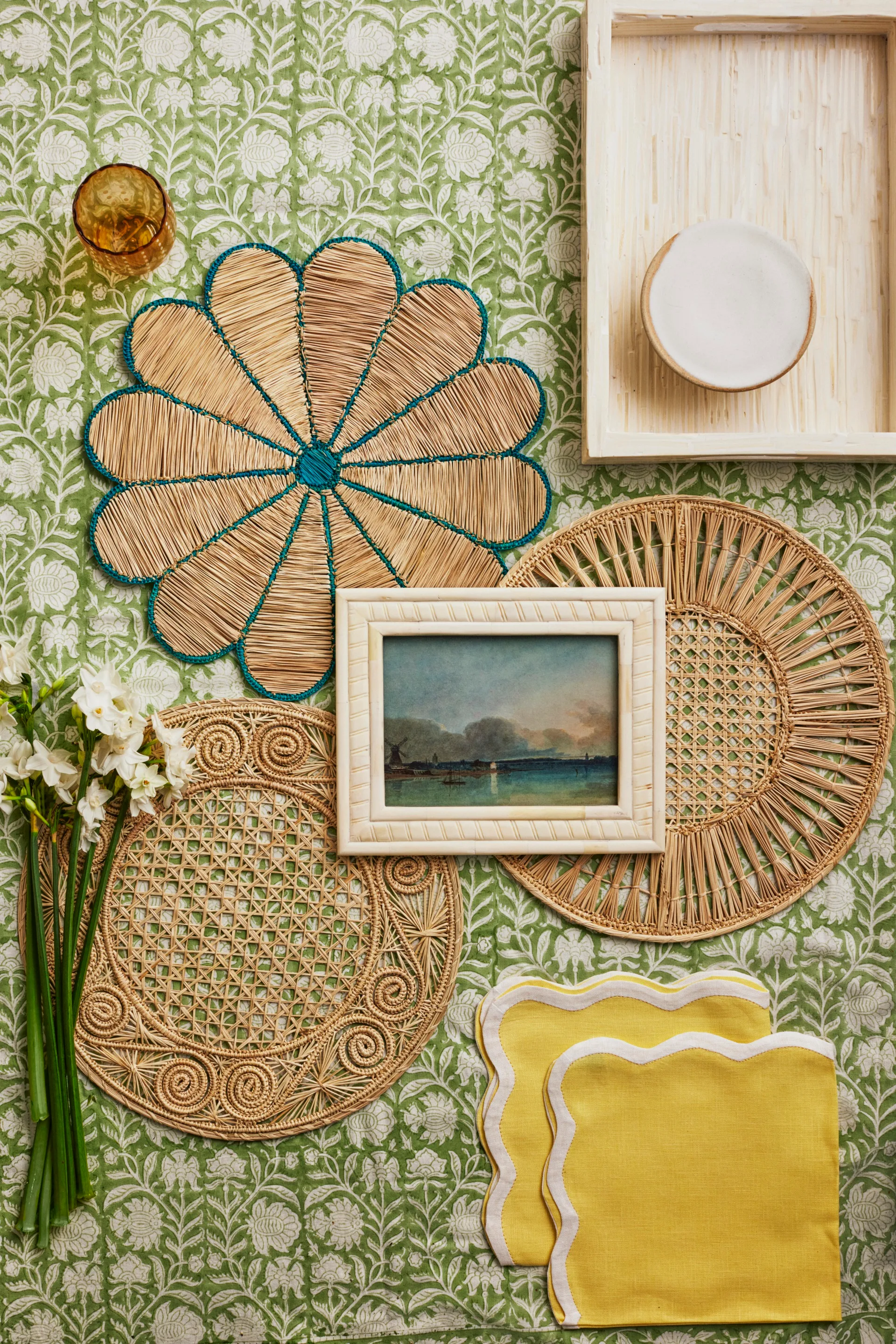 A collection of wicker placemats, yellow napkins and a landscape artwork.