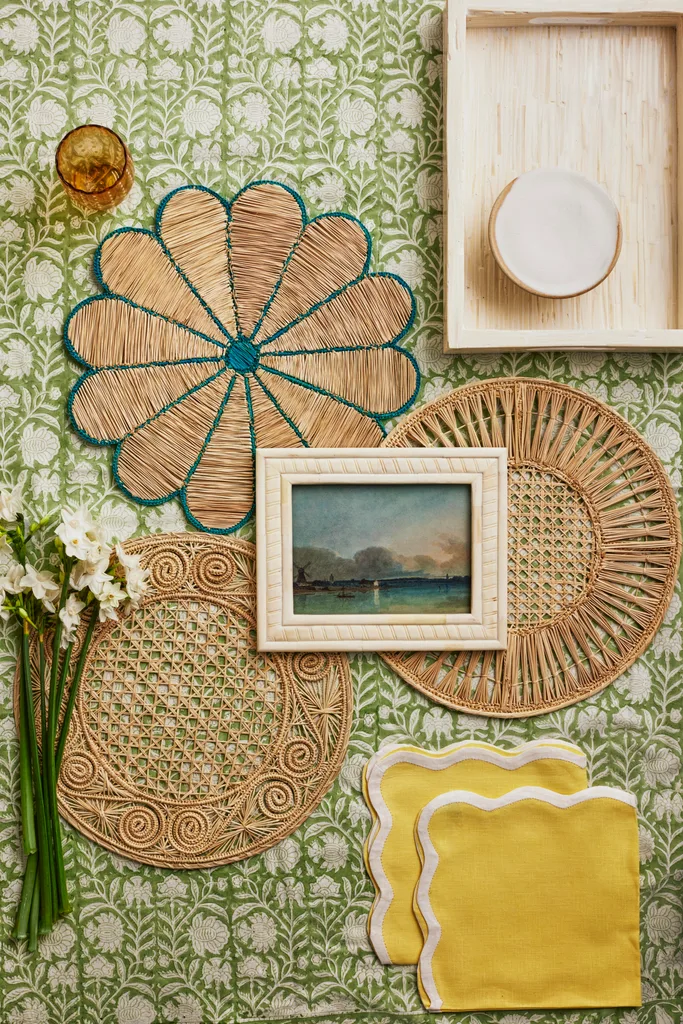 A collection of wicker placemats, yellow napkins and a landscape artwork.