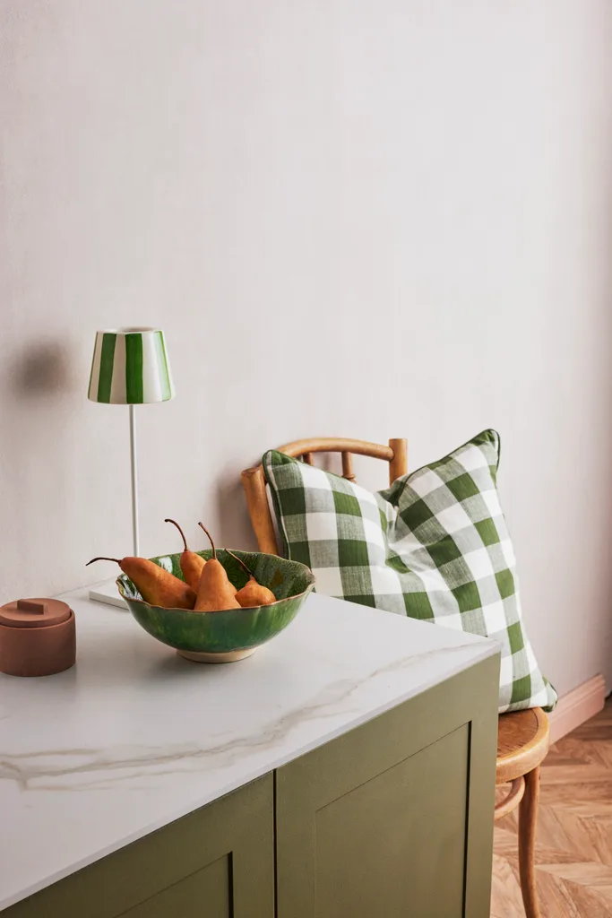 A green bowl of pears on a console beside a chair with a green gingham cushion.