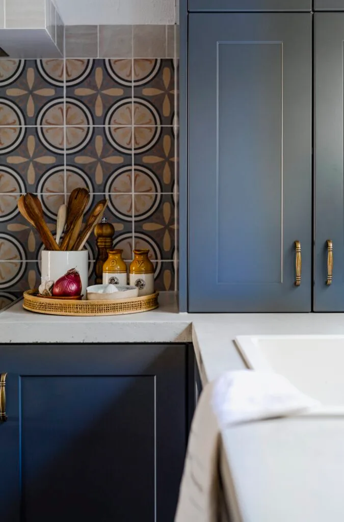 Blue kitchen cabinets with bronze handles next to a mosaic splashback.