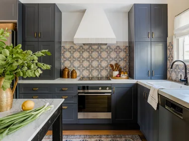 A modern kitchen with blue cabinetry, mosaic splashback tiles and marble benchtops.