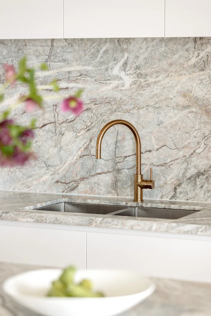 A kitchen sink with gold tapware and grey marble benchtops.