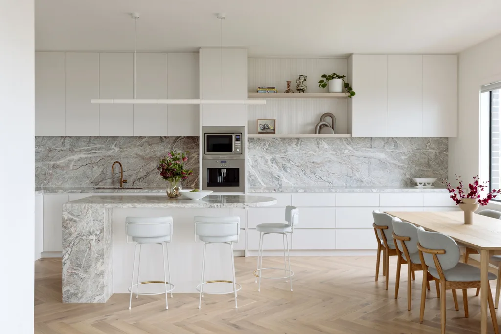 A bright modern kitchen with marble benchtops, an island and a timber dining table.