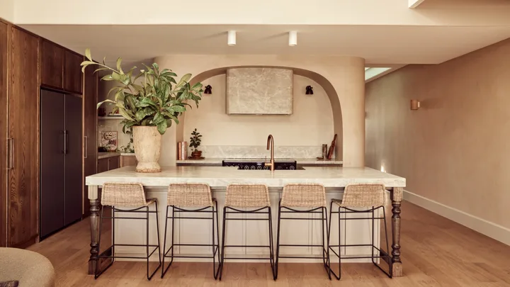 A Spanish resort style kitchen with a large island, woven stools and a curved rangehood.