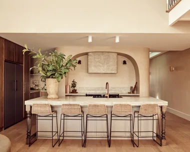 A Spanish resort style kitchen with a large island, woven stools and a curved rangehood.