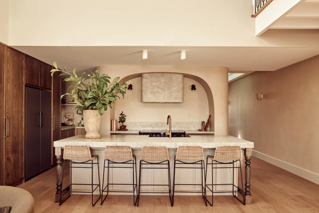 A Spanish resort style kitchen with a large island, woven stools and a curved rangehood.