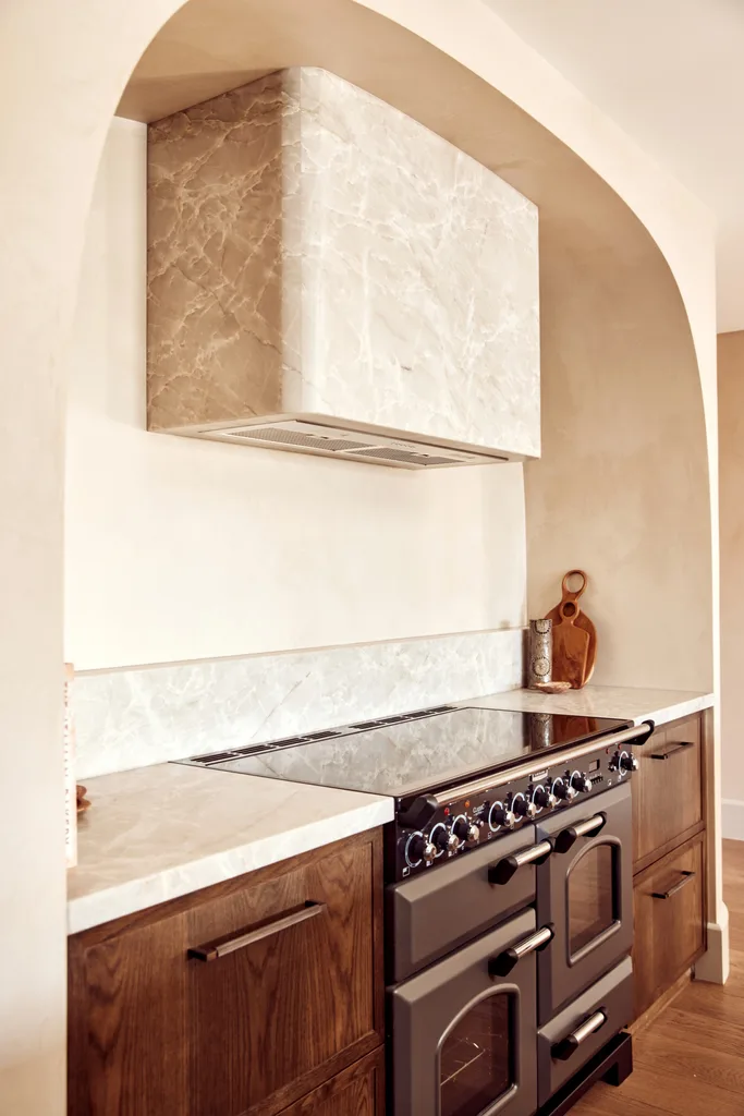 A curved stone rangehood above dark timber joinery.