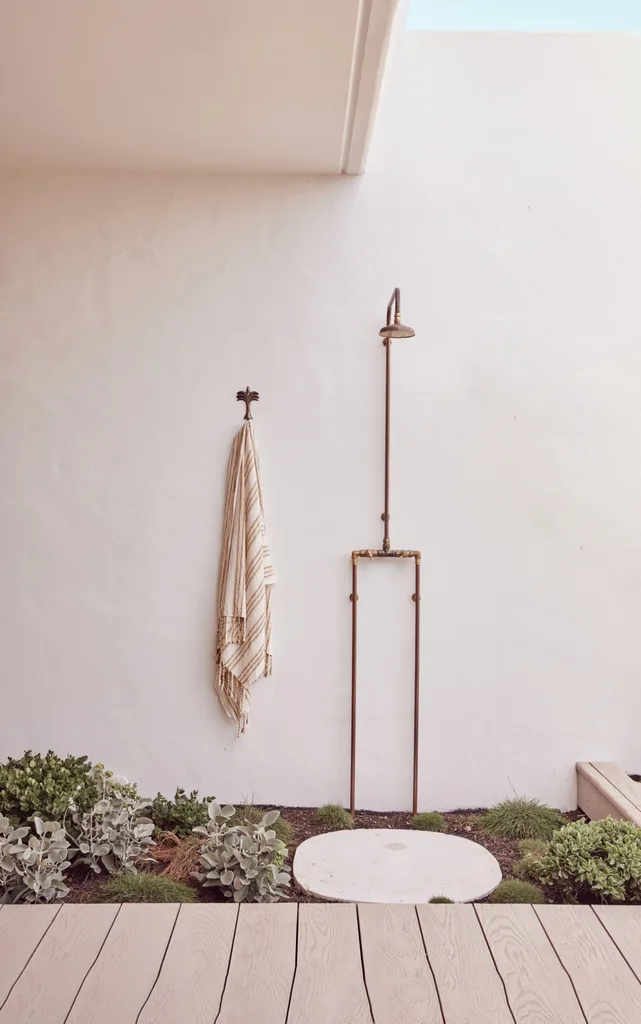 An outdoor shower by a white stucco-style wall.