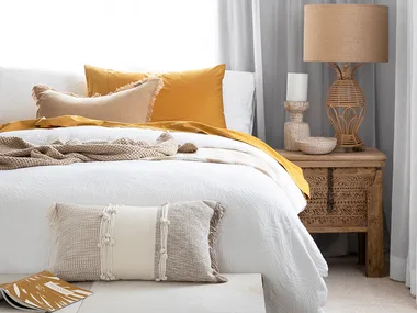 Bedroom setting with sheer curtains an upholstered bench seat at the base of the bed and butter yellow cushions on the bed