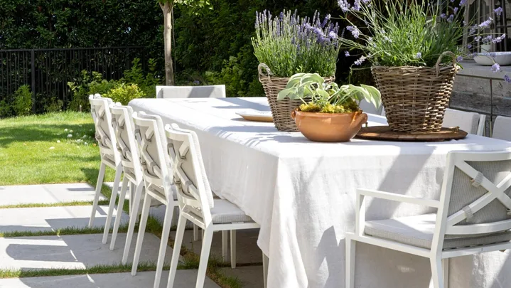 Hamptons style outdoor dining table with a white tablecloth and white dining chairs under string lighting.