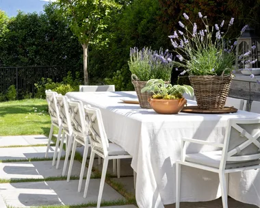 Hamptons style outdoor dining table with a white tablecloth and white dining chairs under string lighting.