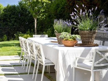 Hamptons style outdoor dining table with a white tablecloth and white dining chairs under string lighting.