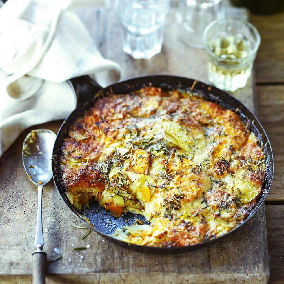 Potato, squash and pumpkin gratin in cast iron pan on serving board with white wine