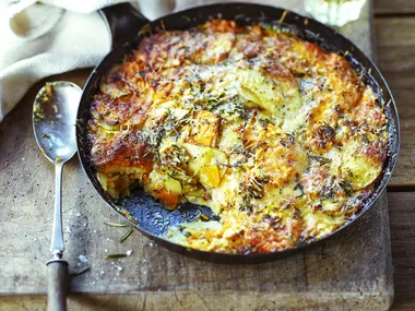 Potato, squash and pumpkin gratin in cast iron pan on serving board with white wine
