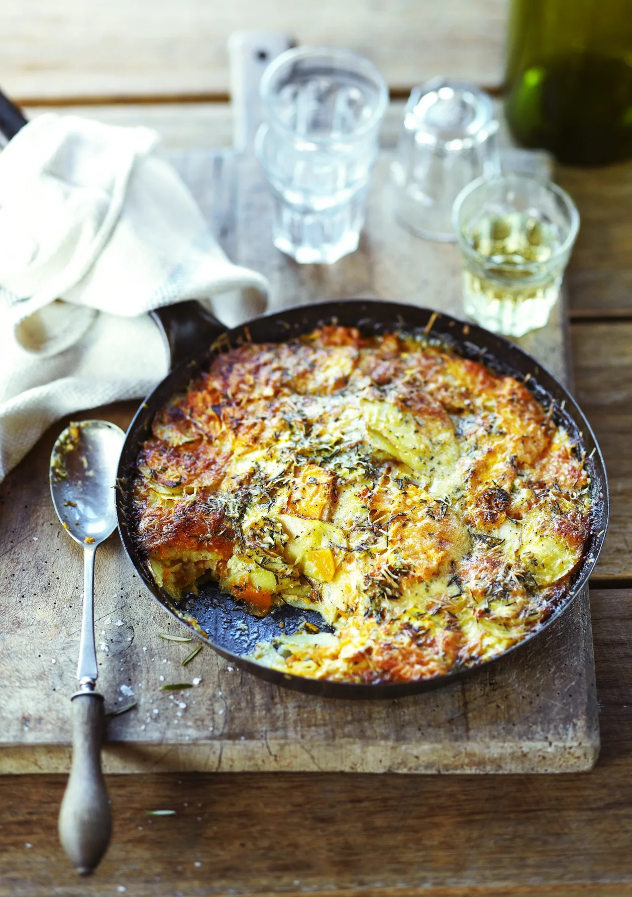 Potato, squash and pumpkin gratin in cast iron pan on serving board with white wine