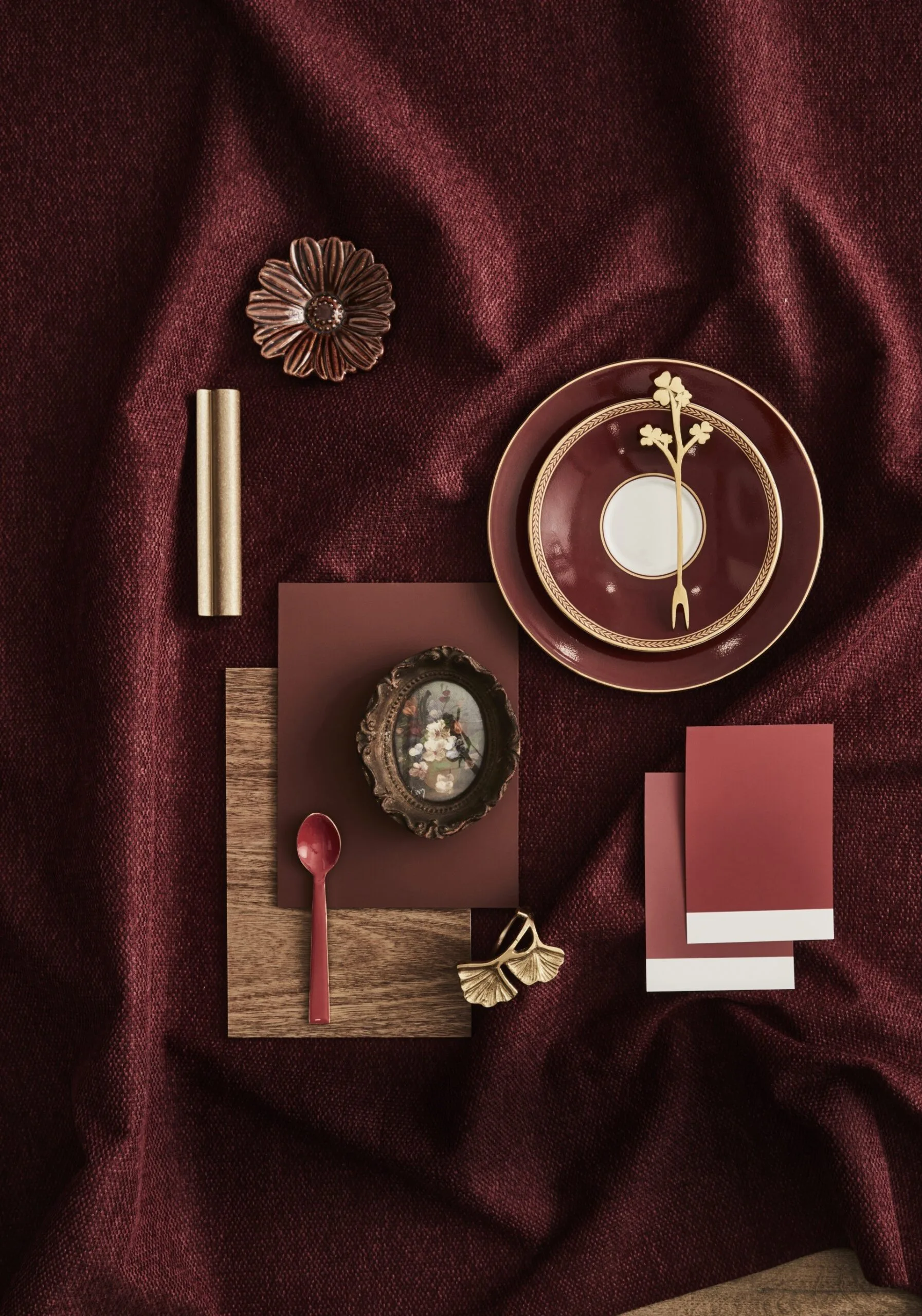 Red cloth with a moodboard of red paint swatches, Choices Flooring and gilded plates on top.
