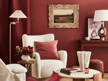 A red wall with a white armchair and a painting in a gilded frame