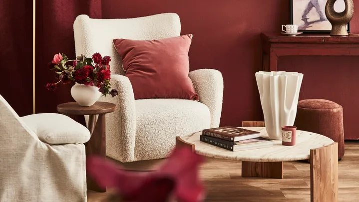 A red wall with a white armchair and a painting in a gilded frame