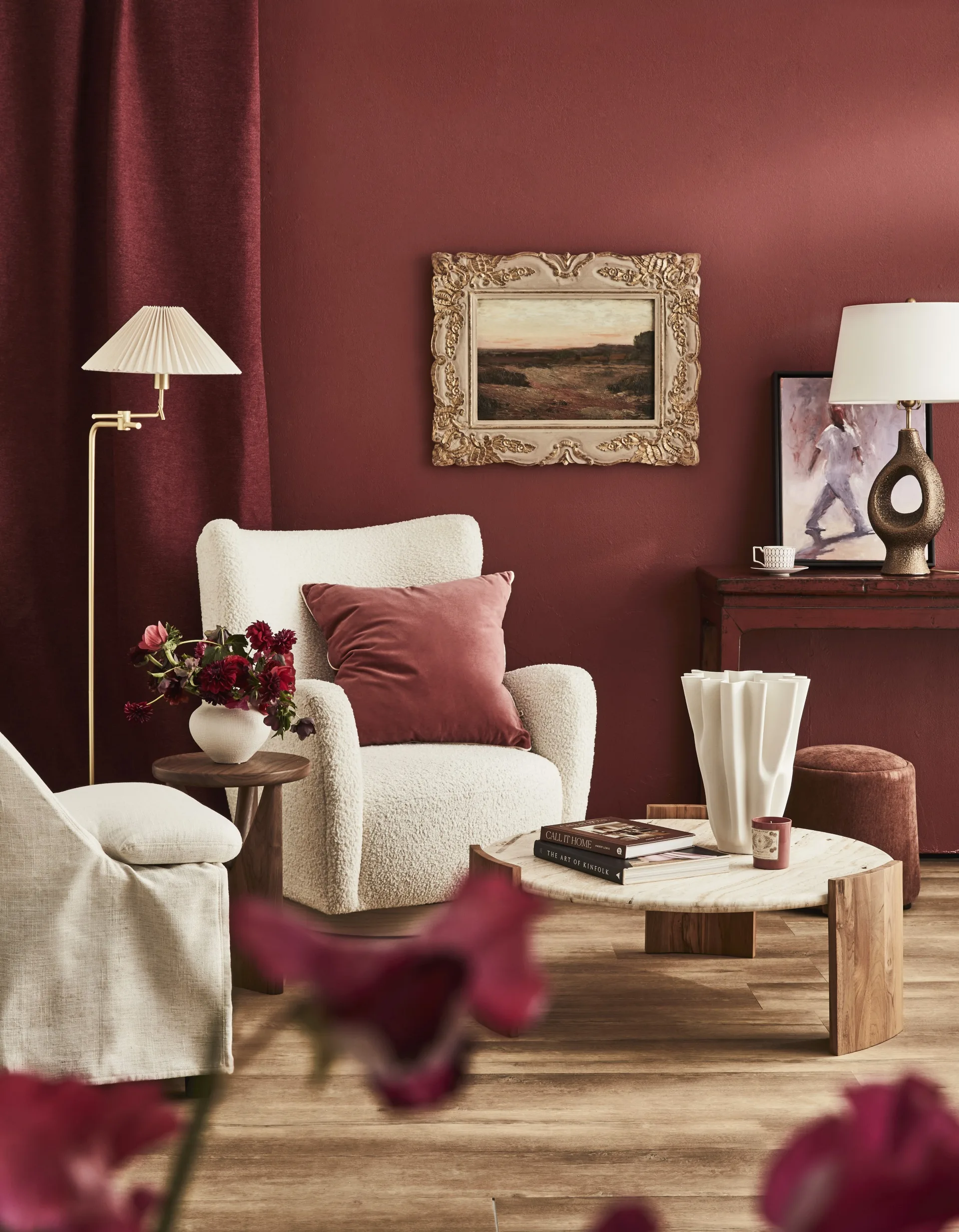 A white armchair against a red wall with a painting in a gilded frame.