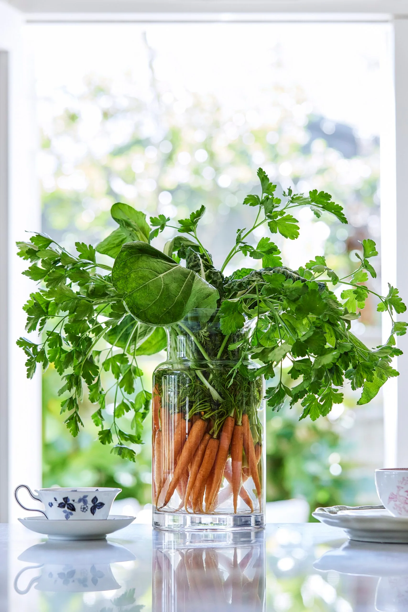 A vase houses an arrangements of carrots with two teacups on either side in this garden inspired kitchen display