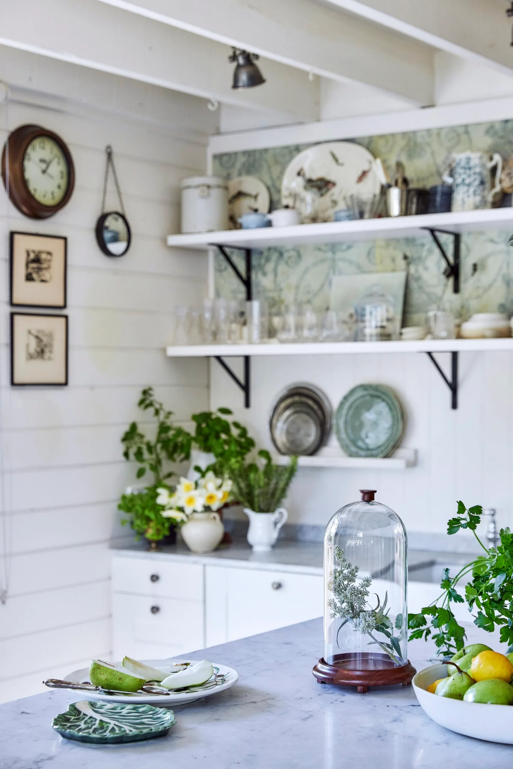 A white kitchen with wooden panelled walls, wallpaper, open shelving and visible beams on the ceiling.